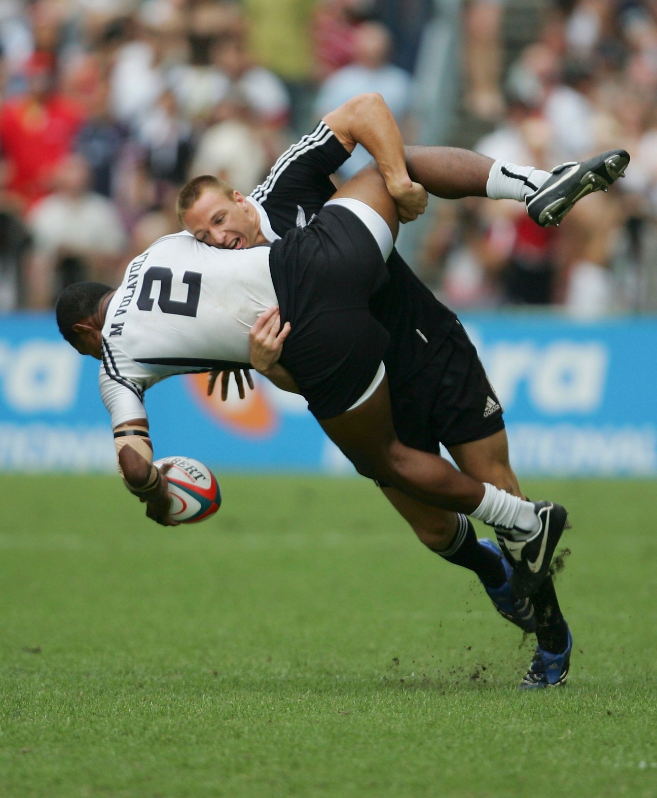 Rugby player in black jersey being tackled by player in white jersey during match.