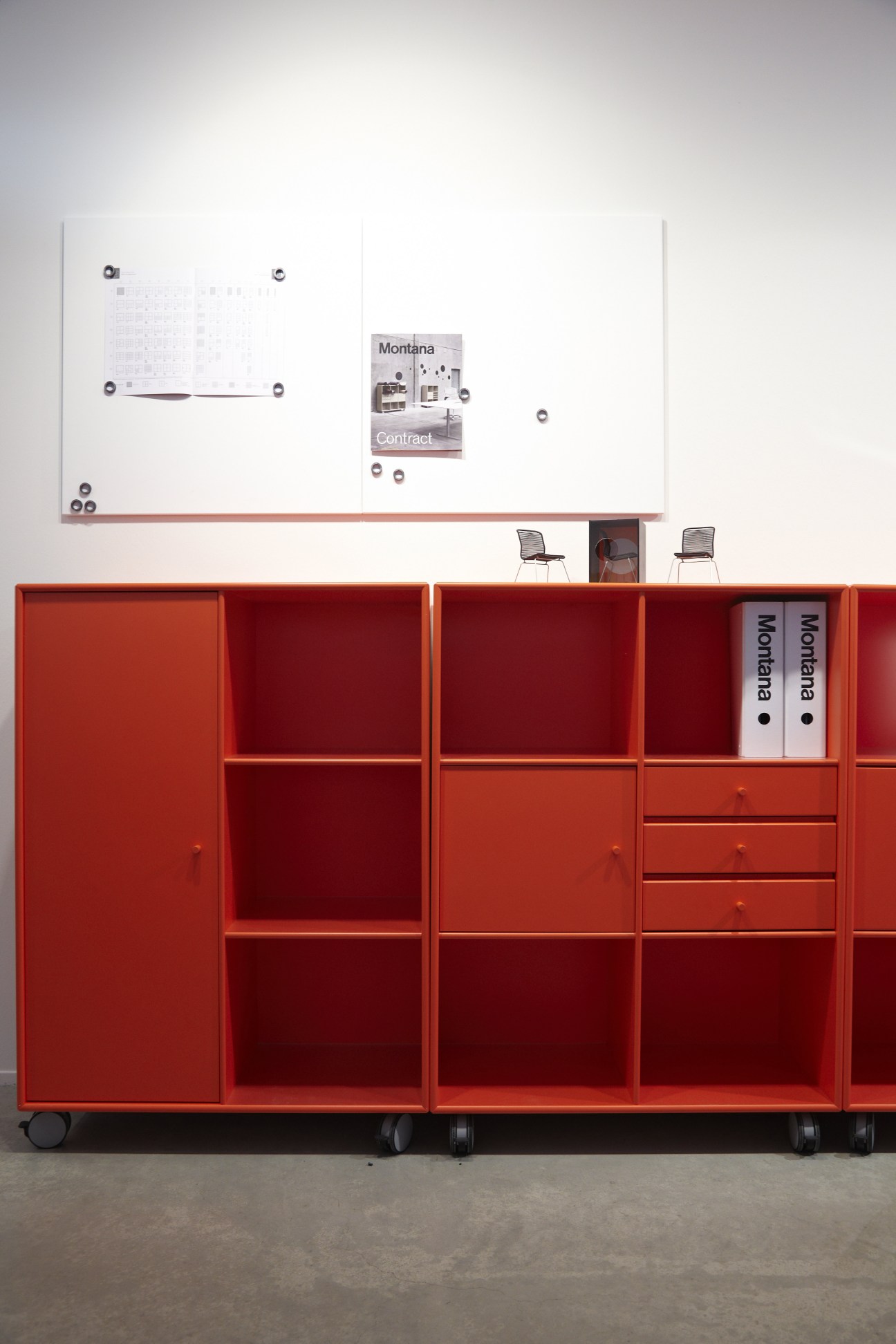 Montana modular storage system in red with open shelving, closed cabinets, and drawers displayed at a trade show.