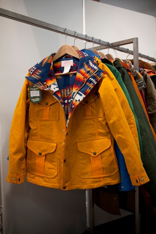 Filson's 1970s hunting-inspired jackets displayed on a rack, featuring a yellow waxed cotton jacket with colorful geometric patterned lining.