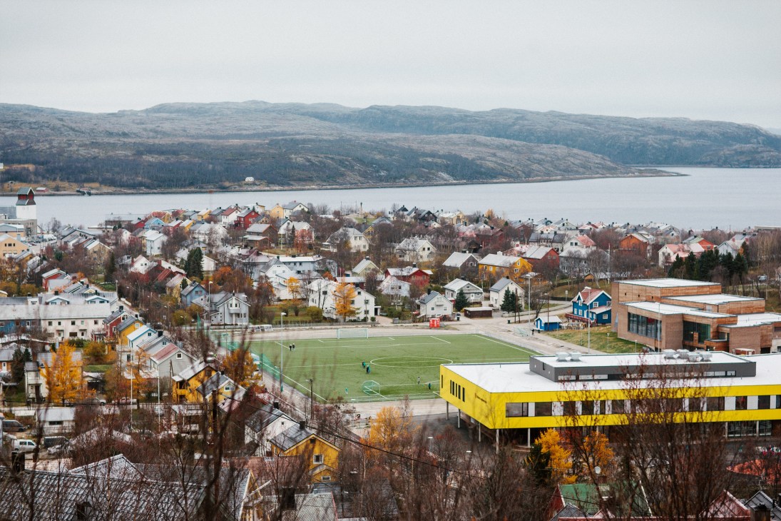 Aerial view of Kirkenes showing colorful houses, a yellow school building, fjord and mountains.
