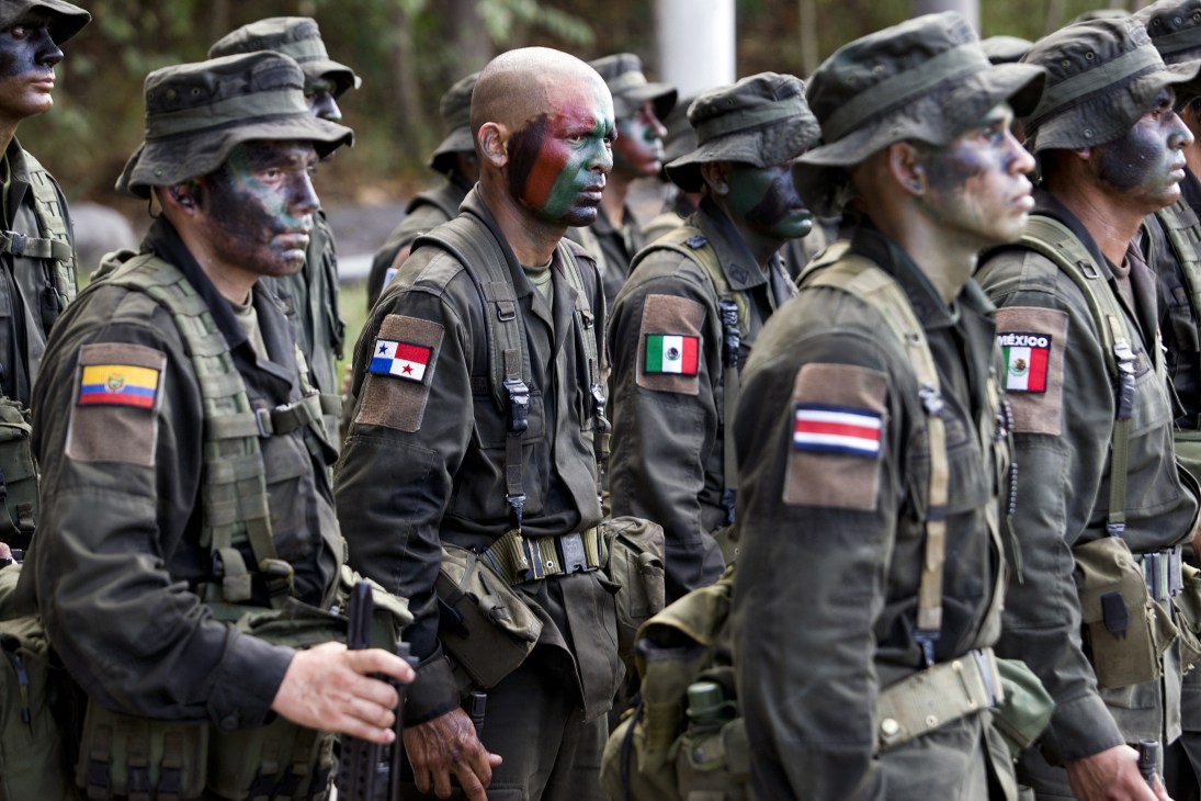 International police and military trainees in camouflage uniforms with face paint, wearing country flag patches from Ecuador, Panama, Mexico and Costa Rica.