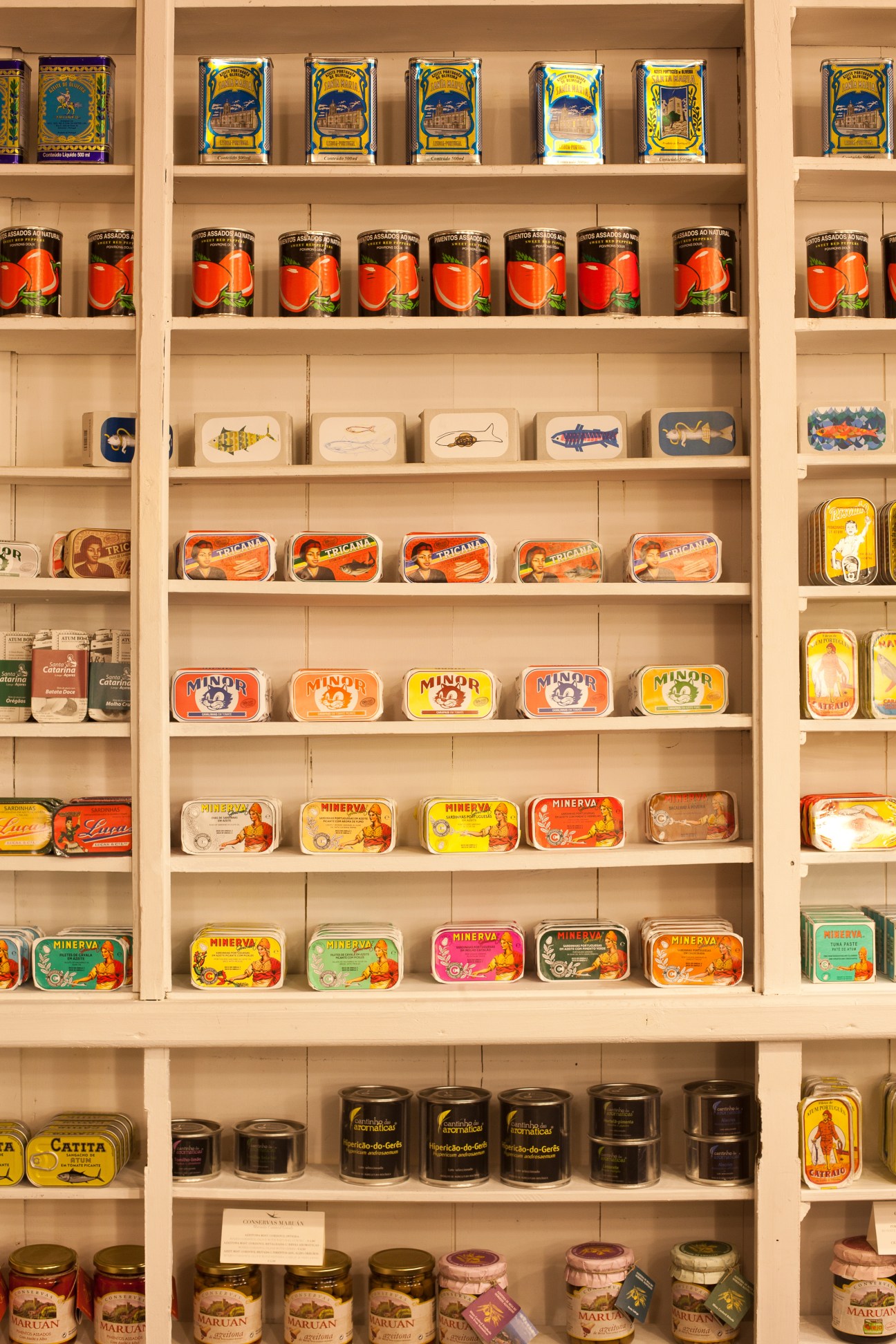 Wooden shelves displaying vintage Portuguese product packaging including sardine tins, soaps, and traditional branded boxes.