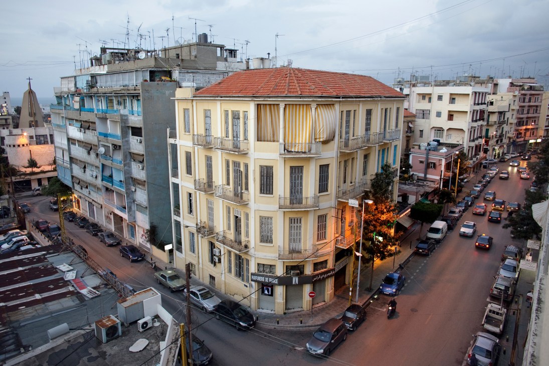 Aerial view of Mar Mikhael neighbourhood showing yellow corner building with red tile roof among other residential buildings and parked cars on street.