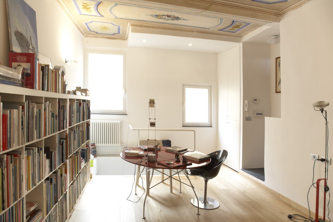 Modern apartment interior with built-in bookshelves, desk, and ornate ceiling moldings in Camogli.