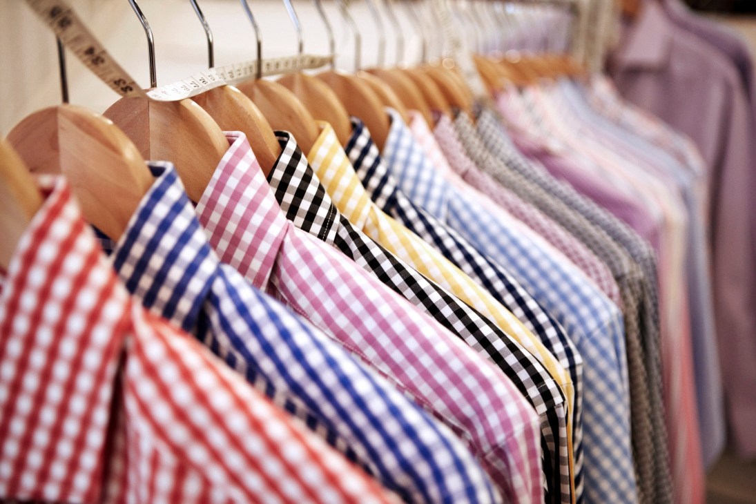 Colorful striped shirts hanging on wooden hangers with measurement tape visible.