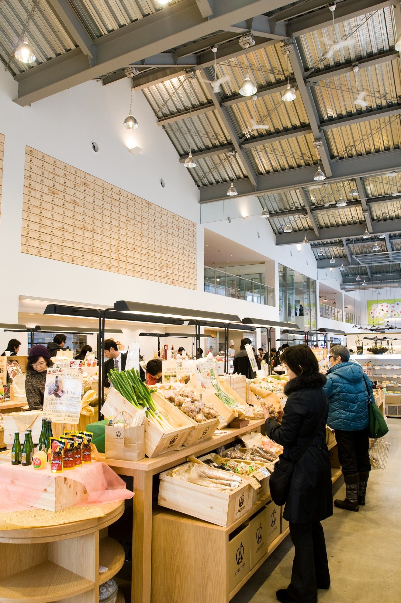 Interior of Food Marché at A-Factory showing shoppers browsing wooden market stalls with local produce under industrial ceiling.