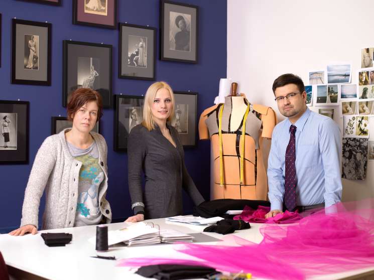 Three people stand beside a dress form mannequin with measuring tape in a design studio.