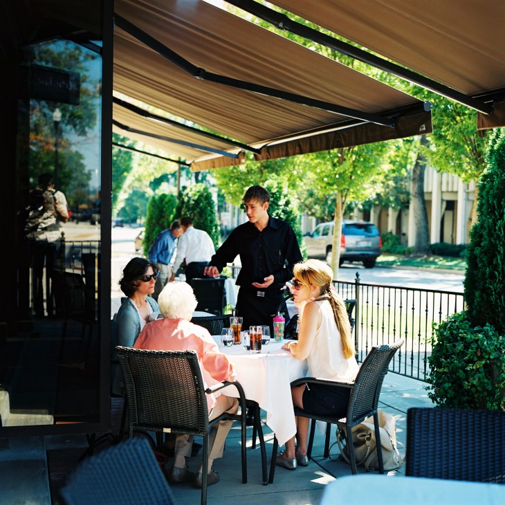 Diners seated at tables under a retractable awning on the patio of Cotton Row restaurant in Huntsville.