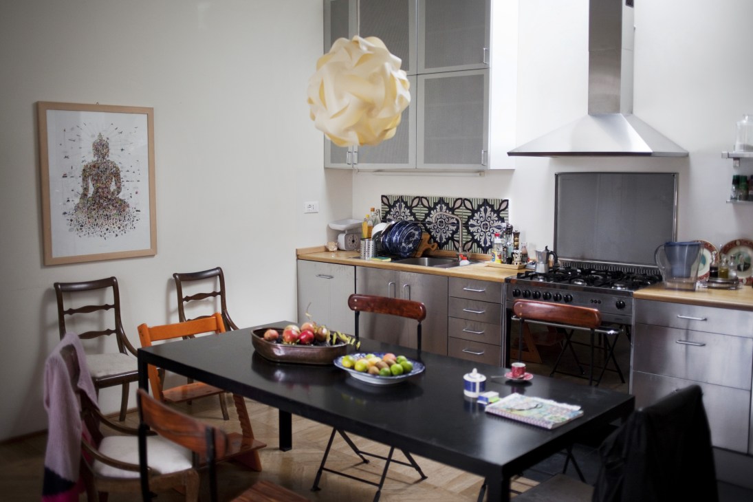 Modern kitchen and dining area with black table, mid-century chairs, and contemporary pendant light in Ilaria Freccia's Esquilino home.