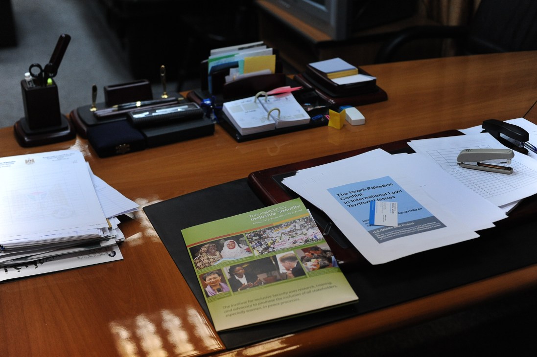 Saeb Erakat's wooden desk at his Ramallah office with documents, office supplies, and books on Palestinian law and security.