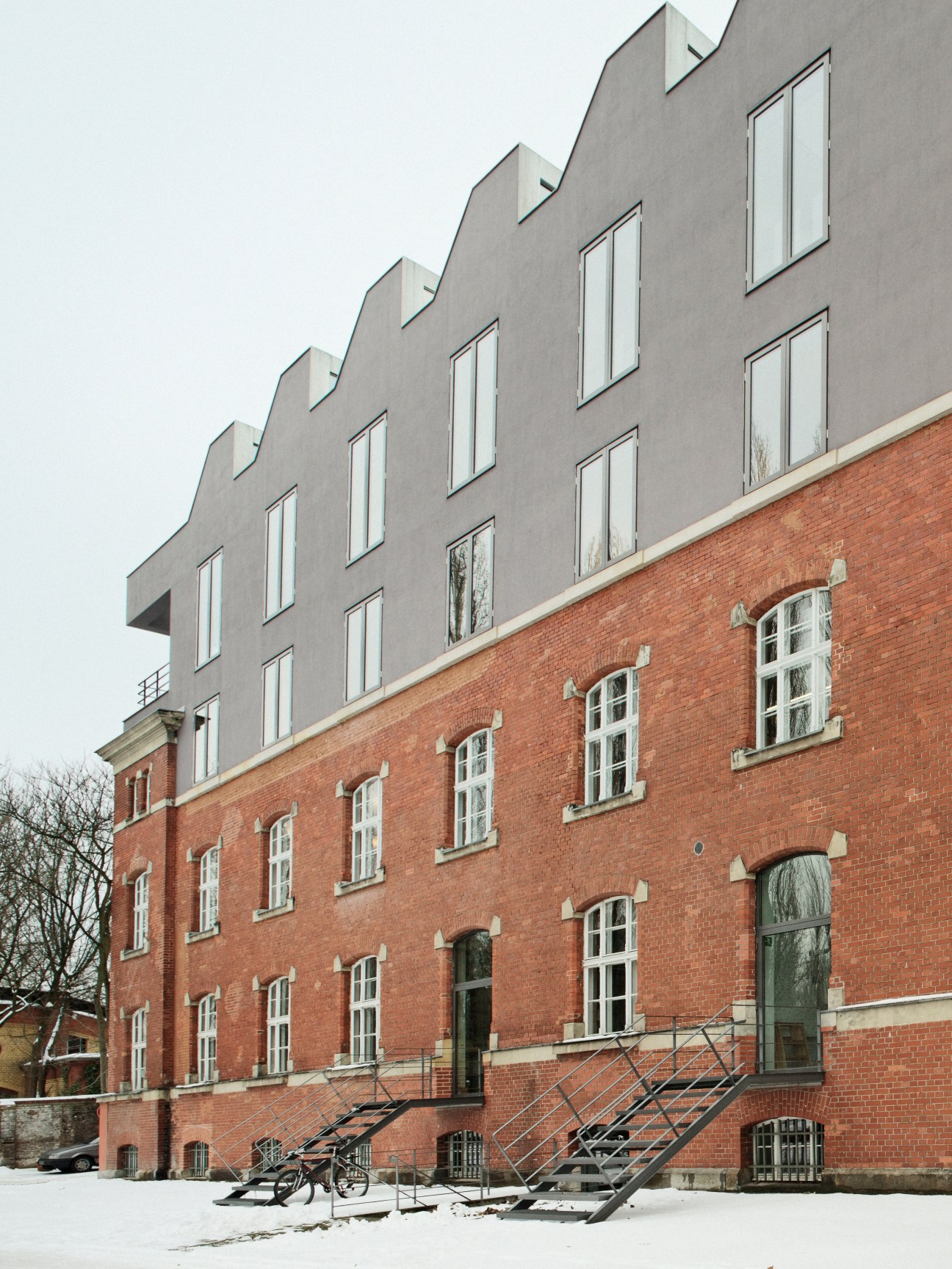 Red brick Prussian Army barracks building with modern grey extension on top featuring zigzagged roof and ceiling windows.