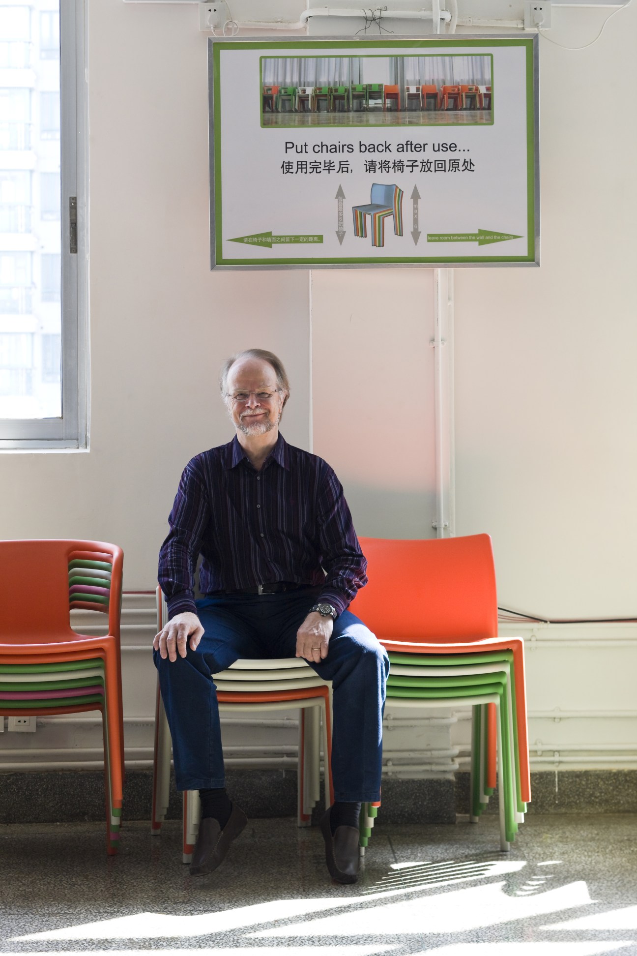 Yrjö Sotamaa, executive vice director of the Sino-Finnish Centre, sits among stacked colorful chairs below a bilingual instructional sign at the Aalto-Tongji Design Factory in Shanghai.