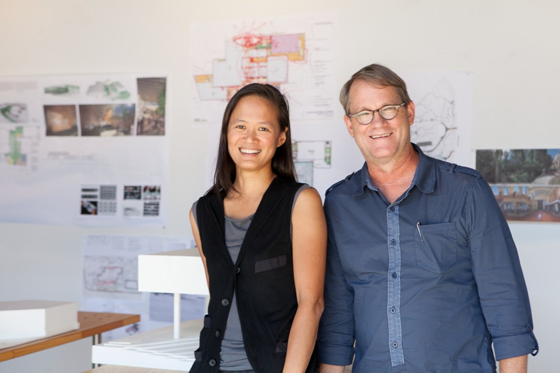 Anne Chen and Gary Carlough stand together at Edge Studio with design plans on the wall behind them.