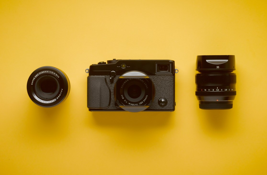 Fujifilm X-Pro 1 camera with interchangeable lenses displayed on yellow background.