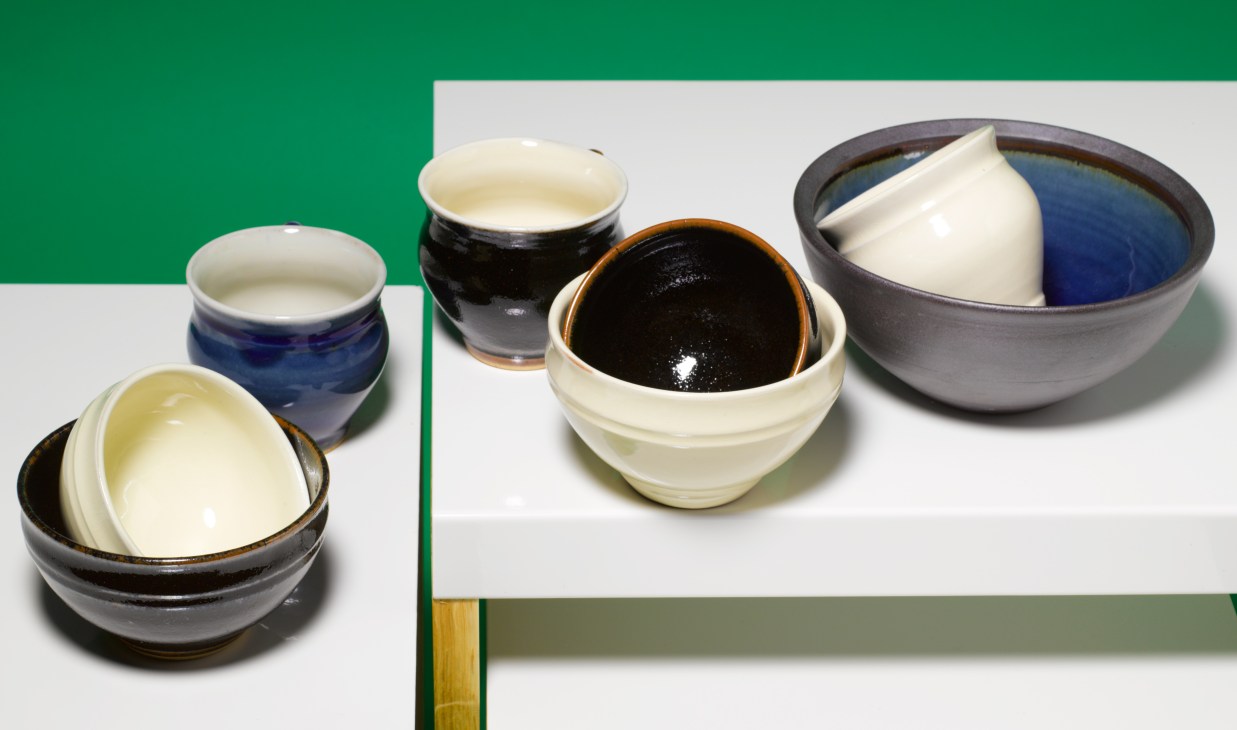 Handmade ceramic bowls with dark and cream glazes displayed on a green and white background.