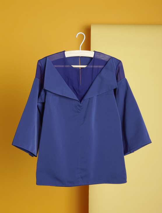 Navy blue silk blouse with three-quarter sleeves and draped collar on white hanger against yellow background.
