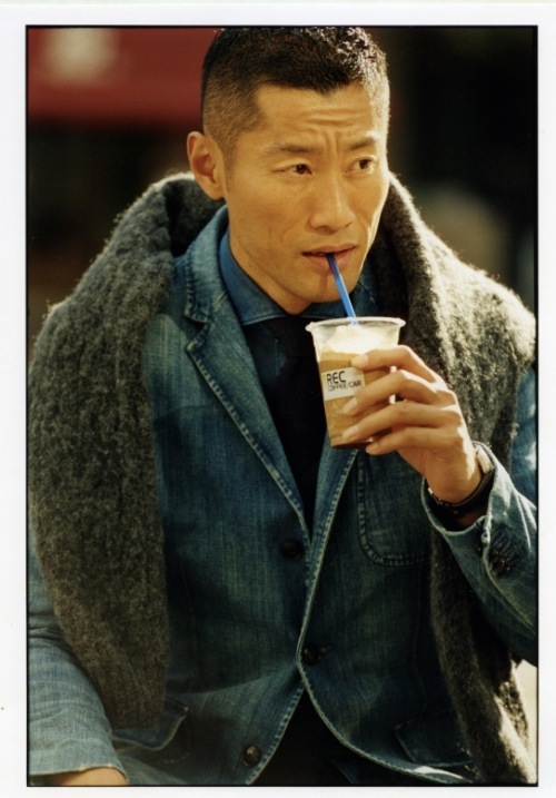 Model Yusuke wearing a denim jacket by Polo Ralph Lauren with layered pieces, drinking from a cup.