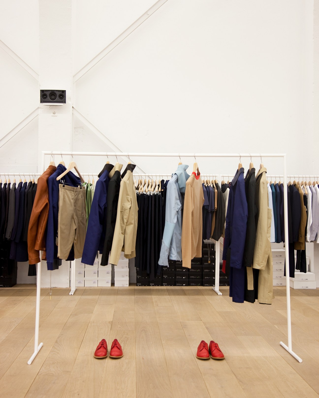 Interior of Andreas Murkudis store in Berlin with clothing rack displaying navy, black, and neutral-toned garments, wooden floor, white walls, and red shoes displayed on ground.