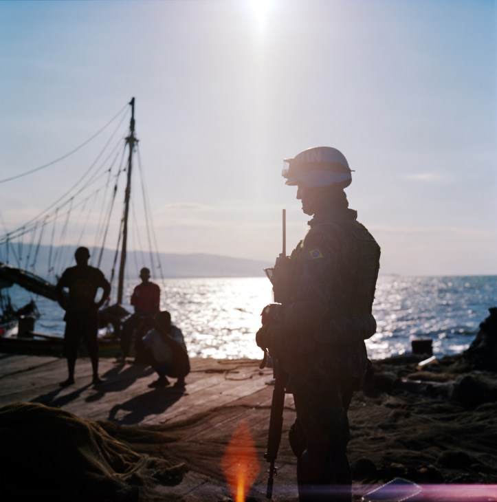 Brazilian soldier on patrol at the waterfront in Cité Soleil, Haiti, silhouetted against the sea at dusk.