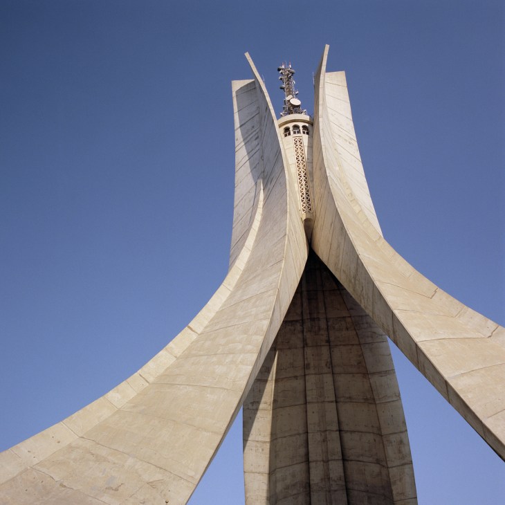 Upward view of Martyrs' Memorial monument with curved white concrete wings and central tower against blue sky.