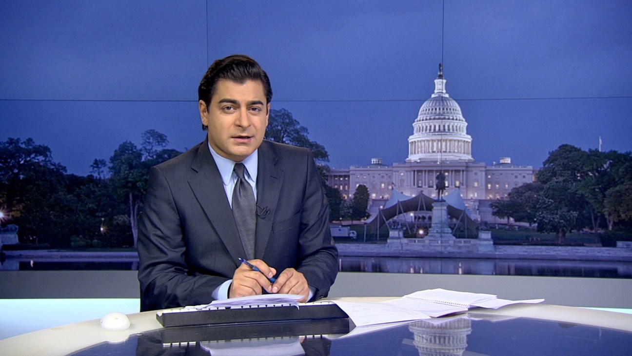 News anchor at desk with Capitol Building visible in background.