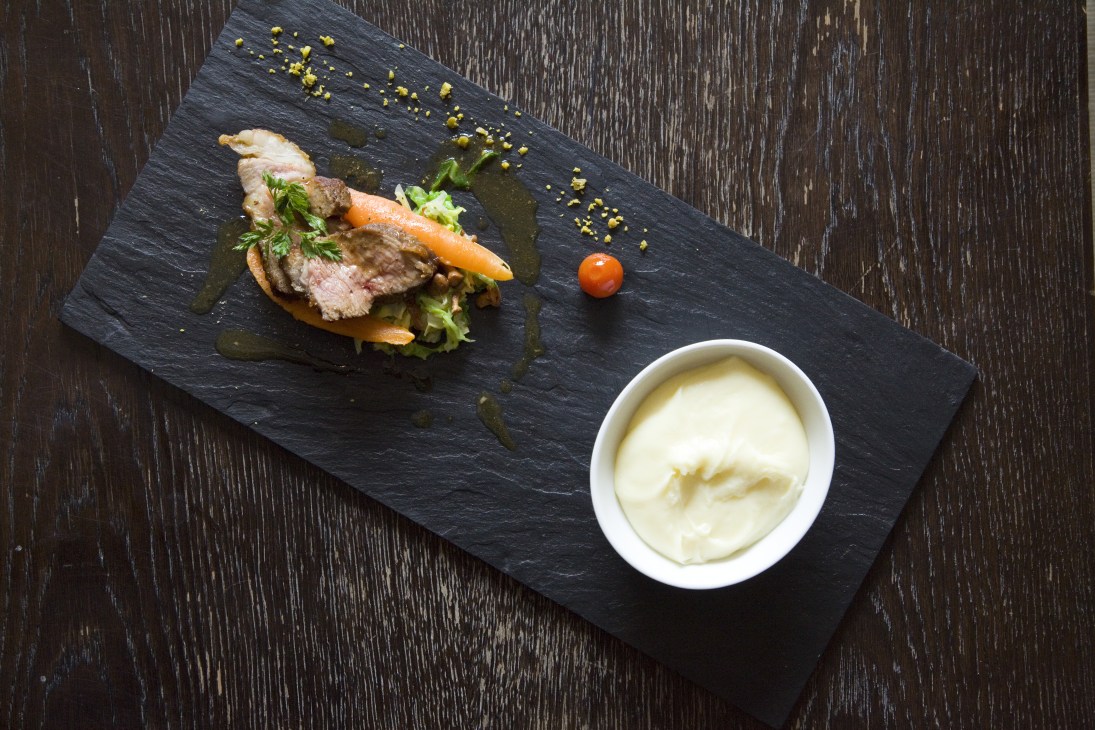 Grilled veal with aligot served on a black slate plate with sauce and garnish.