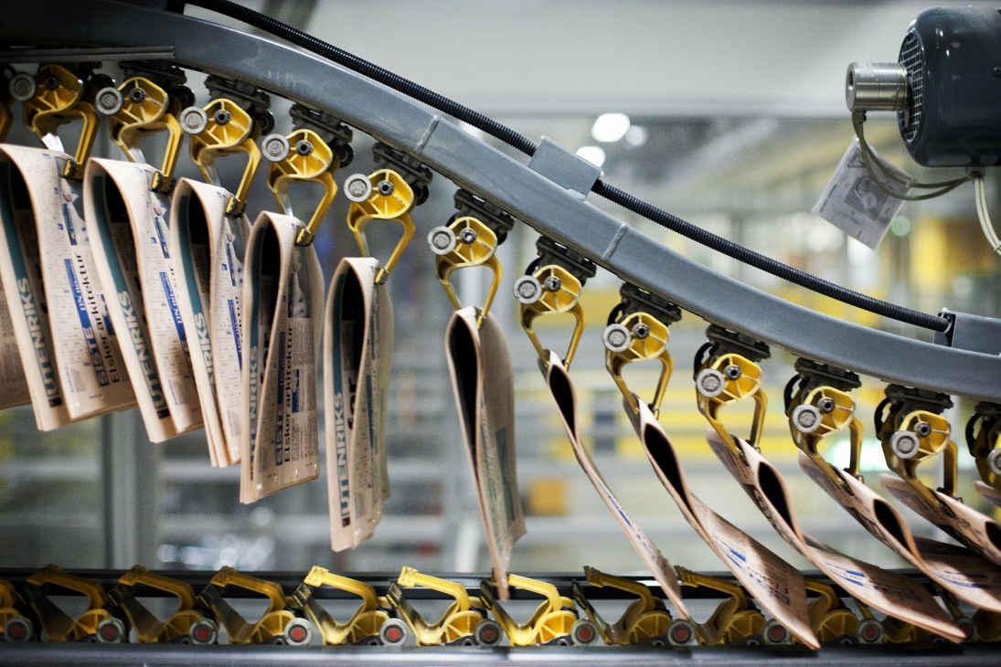 Newspapers on a printing press production line with golden metallic clamps holding them in place.