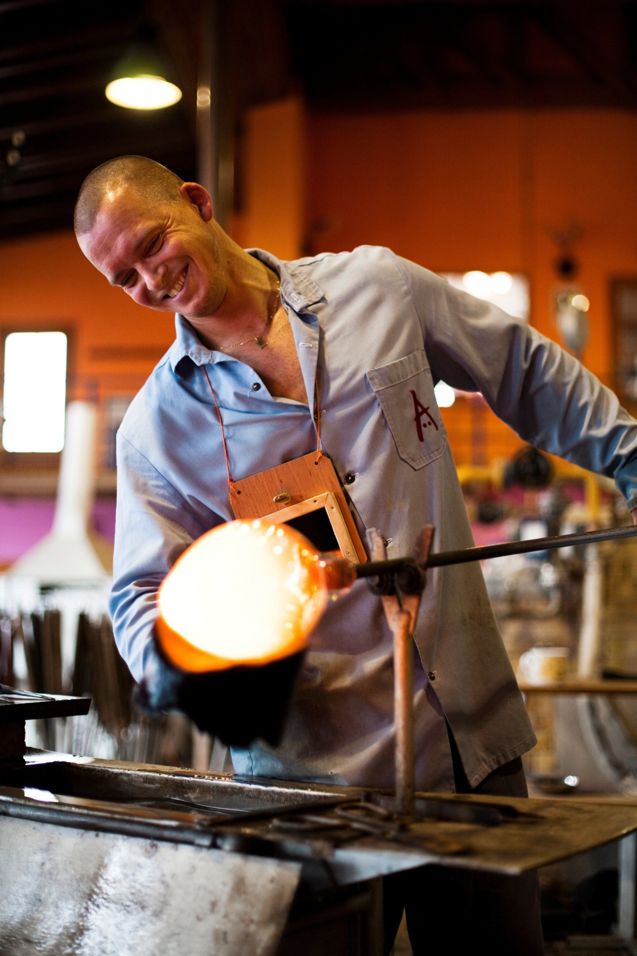 Glassmaker shaping molten glass with tools in the hot shop.