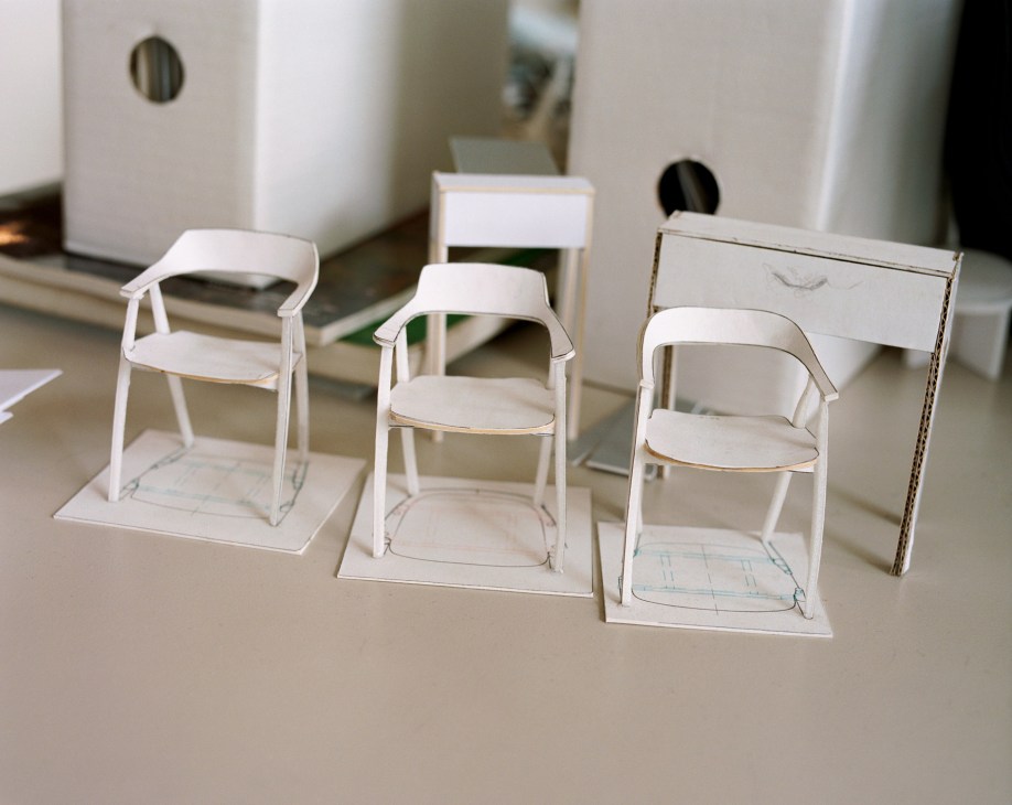 White scale models of dining chairs with curved backrests arranged on a desk.