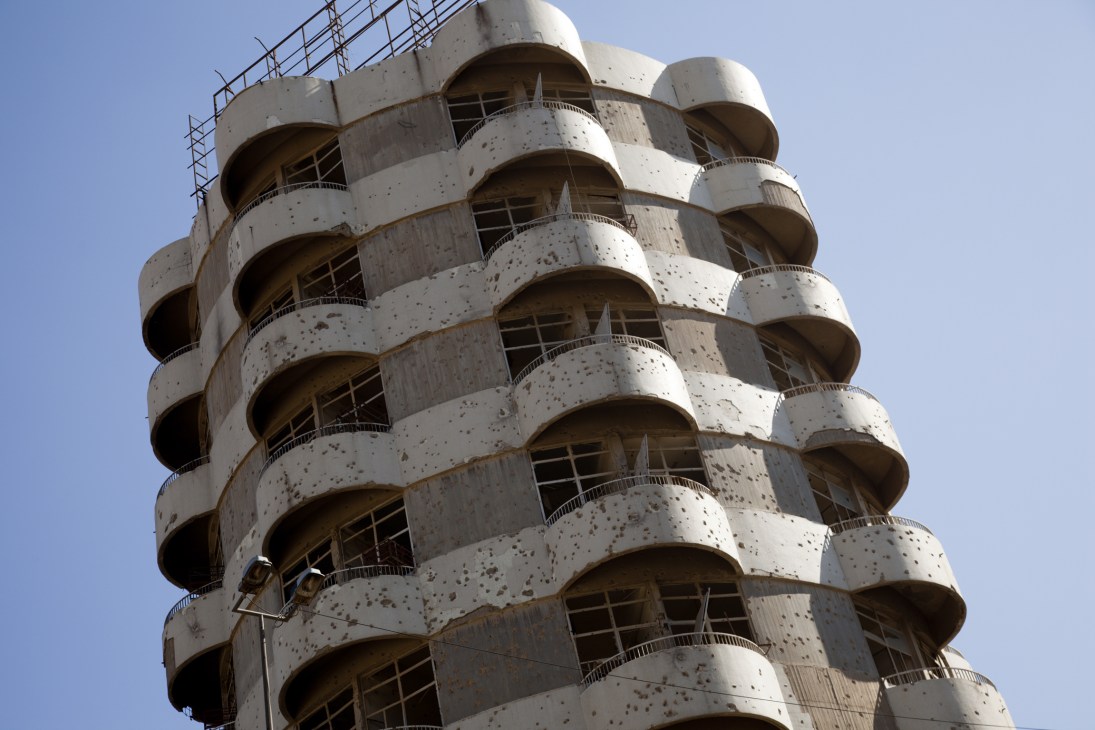 Bullet-scarred concrete tower building with curved balconies showing damage from armed conflict.