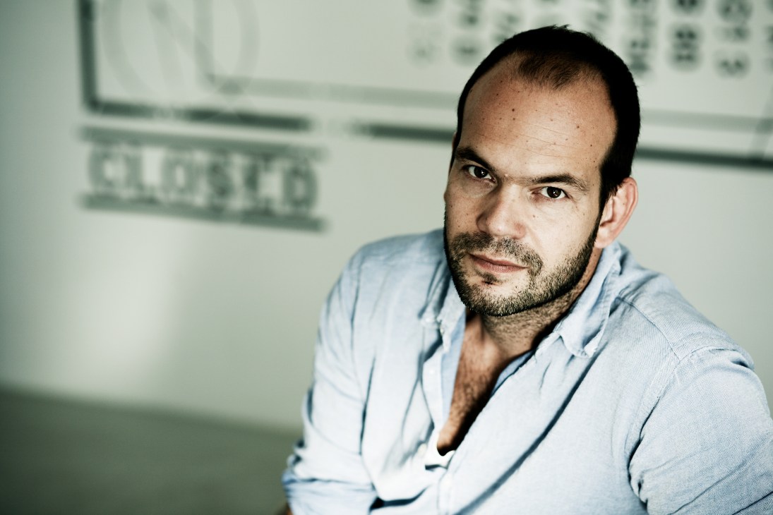 Portrait of Til Nadler, co-founder of Closed, wearing a light blue shirt against a blurred office background.