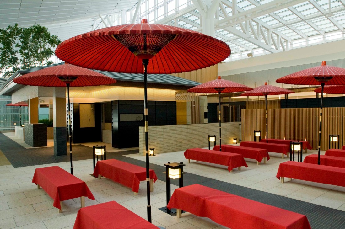 A Japanese-style tearoom with red umbrellas and benches under a skylit ceiling in Haneda's Edo Koji.