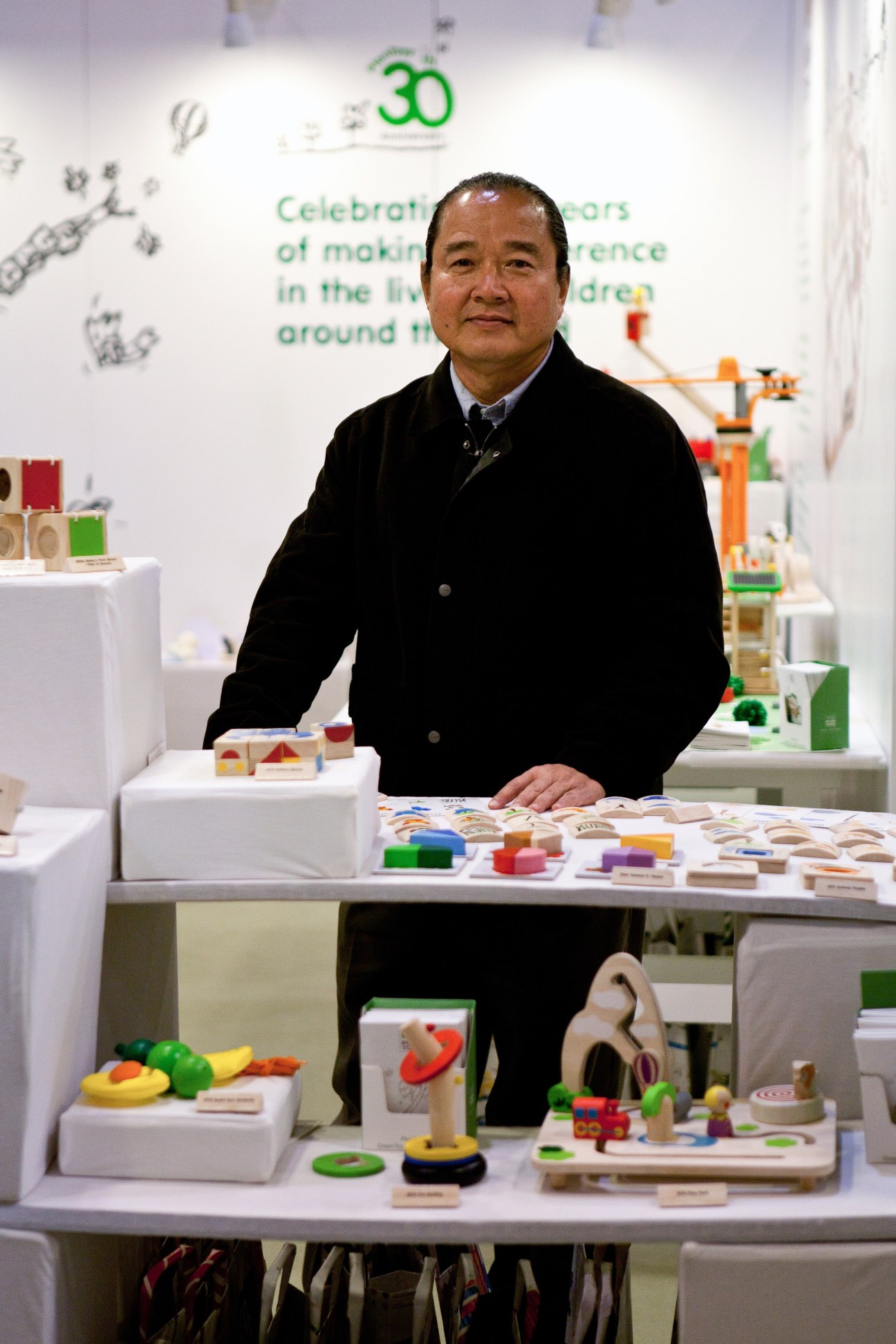 Vitool Viraponsaven, president of Thailand's Plan Toys, stands at a booth displaying colorful wooden toys.