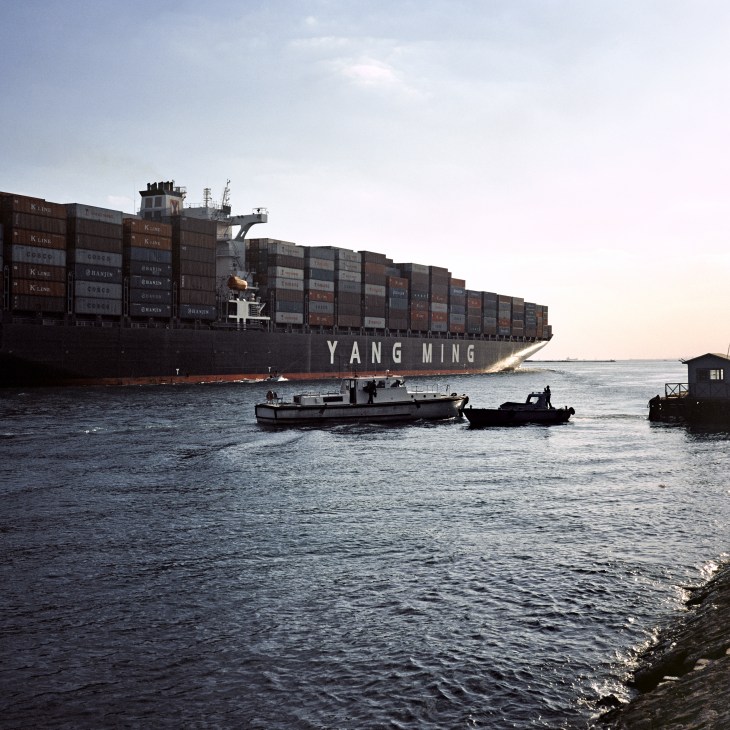 Container ship Yang Ming loaded with cargo passing through the Suez Canal with small boats nearby.