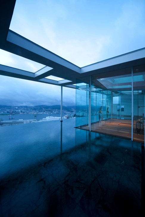 Modern minimalist interior with floor-to-ceiling glass windows overlooking Nagasaki bay at dusk.