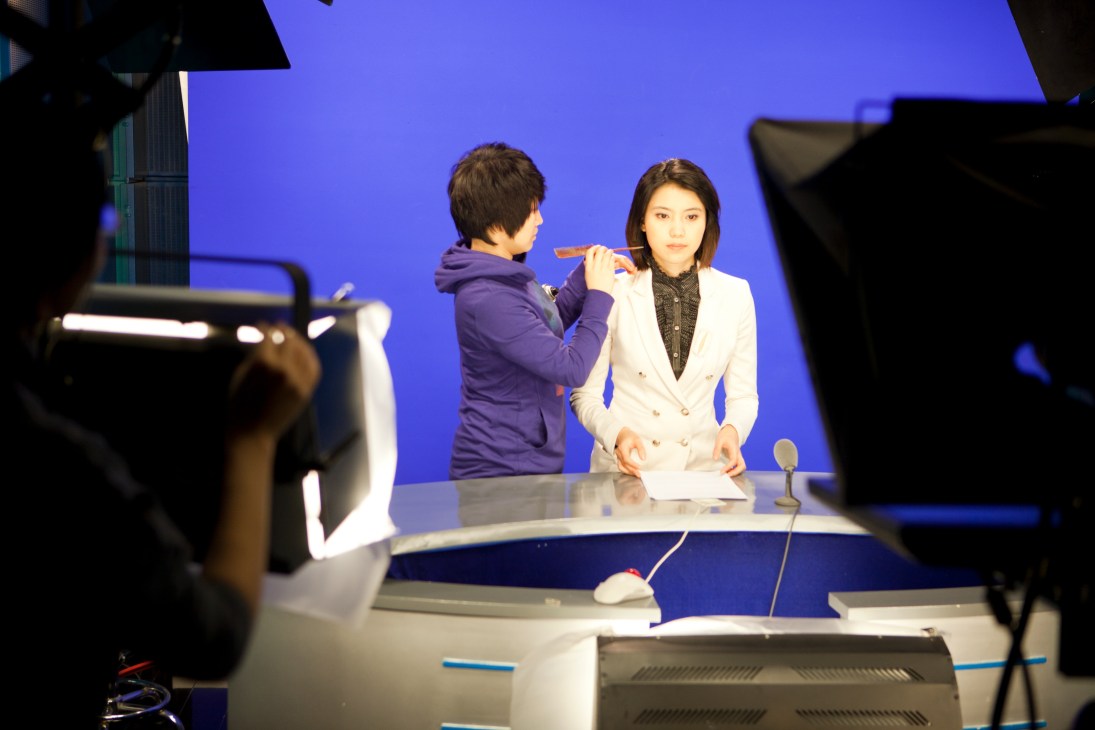 News anchor Nie Danyangzhi receives makeup touch-up before broadcasting at CNC's studio with blue backdrop.