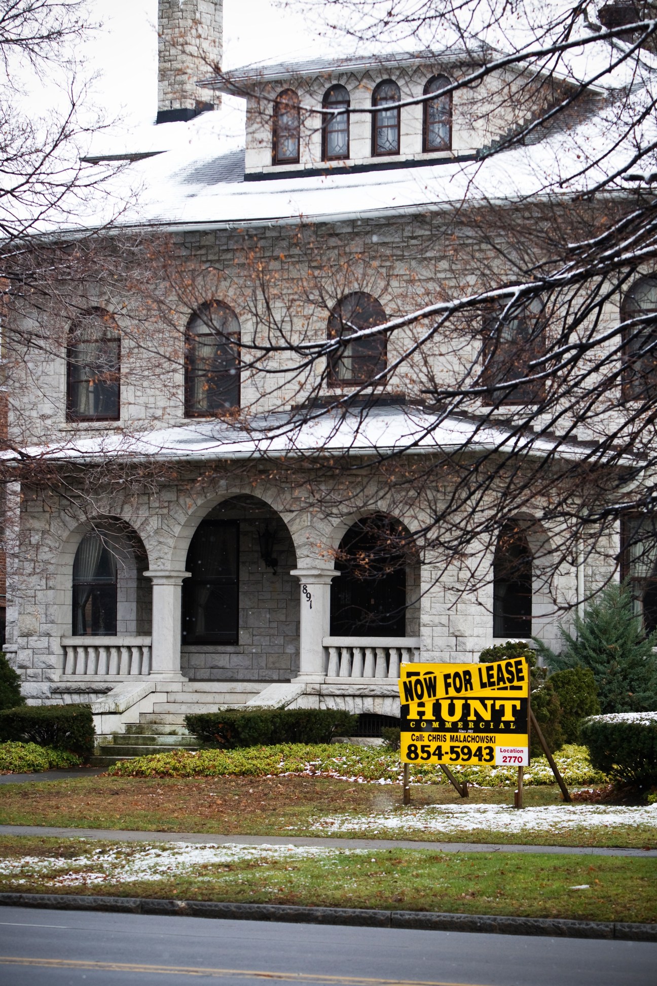 Historic stone mansion on Buffalo's Delaware Avenue with "Now for Lease" sign, bare tree branches, and snow on ground.