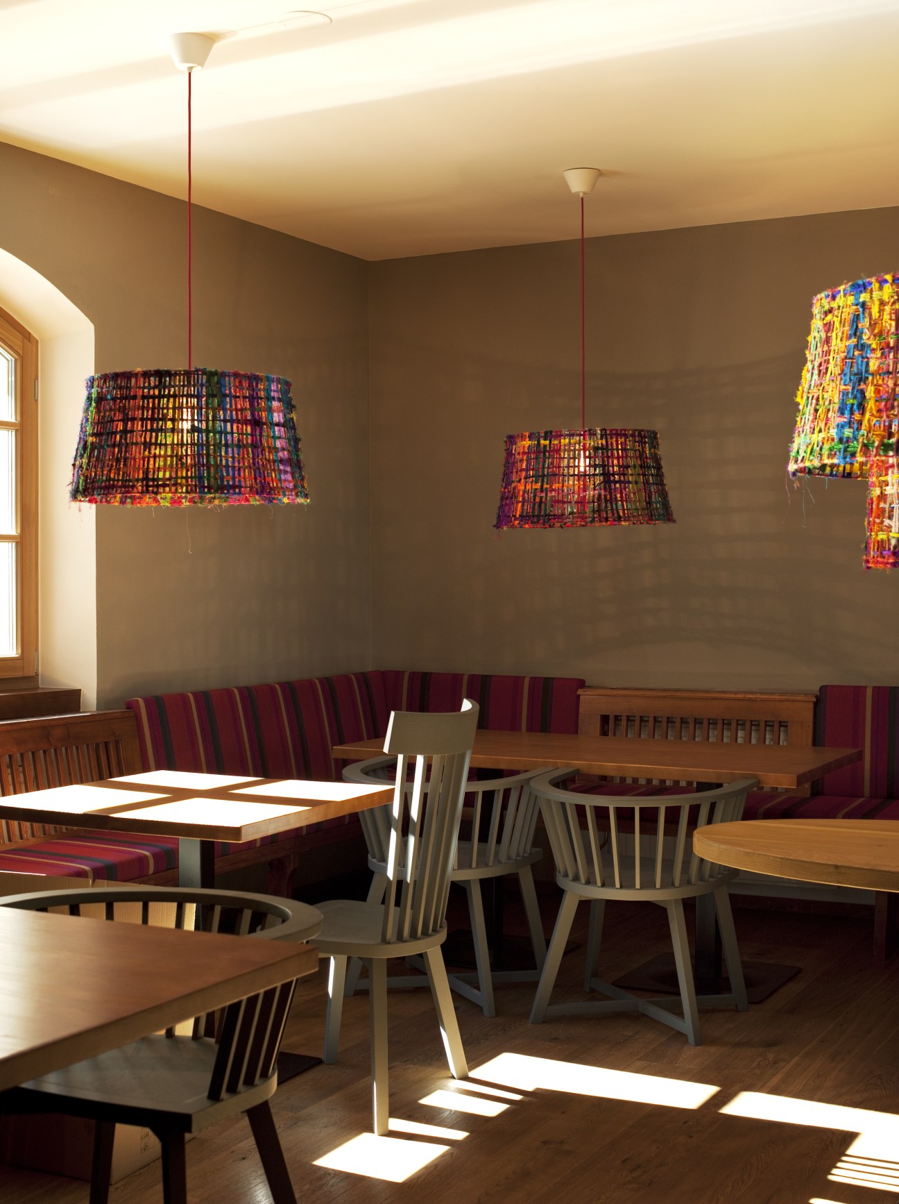 Interior of Valluga Hotel with wooden tables, chairs, and colorful woven pendant lights.