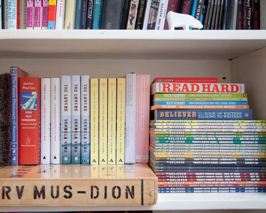 Bookshelf displaying multiple copies of The Believer magazine alongside novels and other books.