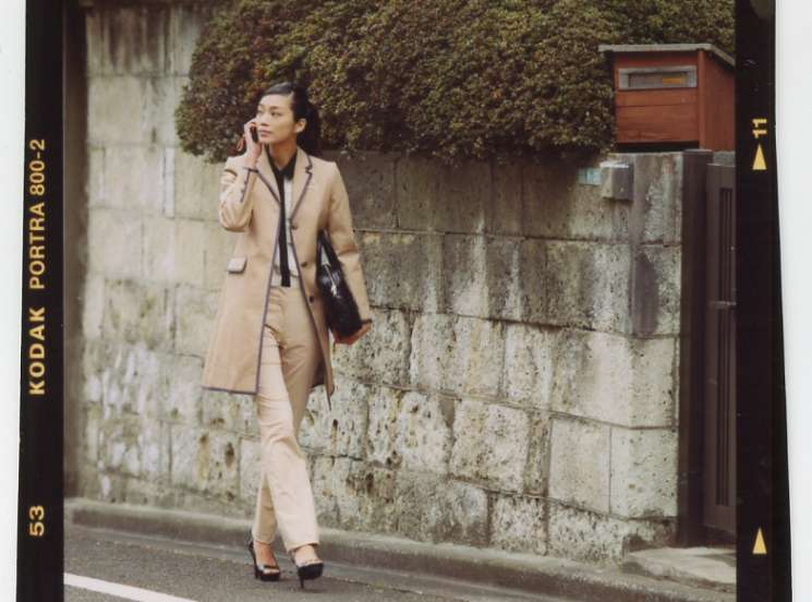 Model in beige coat strolling past ivy-covered stone wall in Tokyo alley
