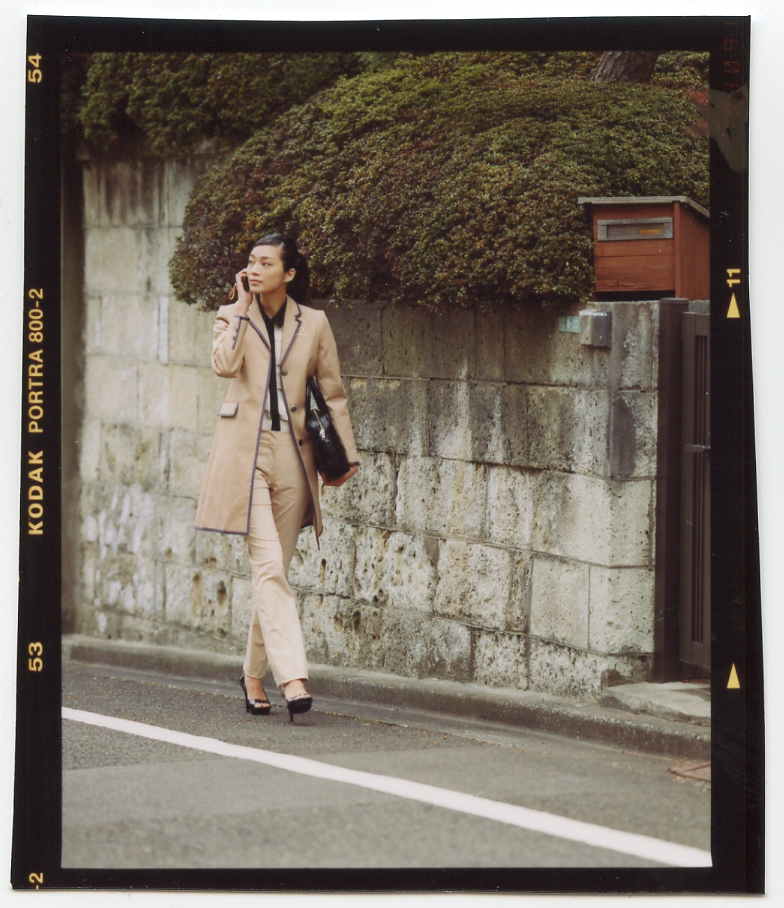 Model in beige coat strolling past ivy-covered stone wall in Tokyo alley