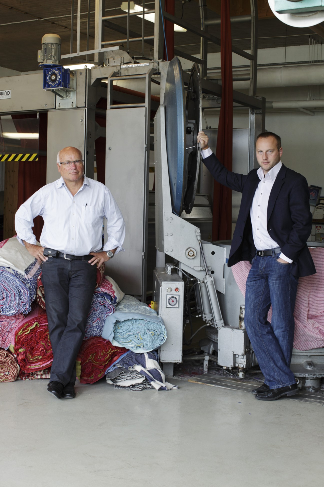 Arnstein and Erling Digernes stand in their Røros-Tweed factory alongside colorful woven blankets and machinery.
