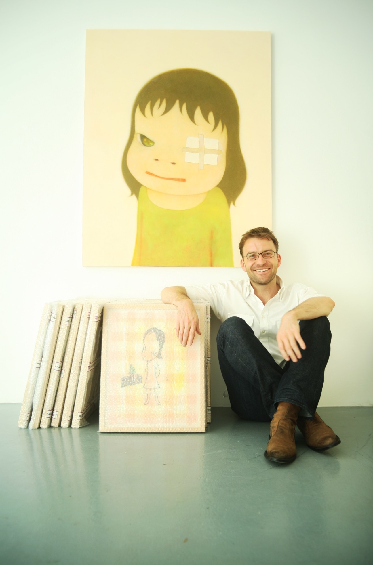 Michael Zink, gallerist, posing with artworks including a painting of a young girl with a yellow dress.