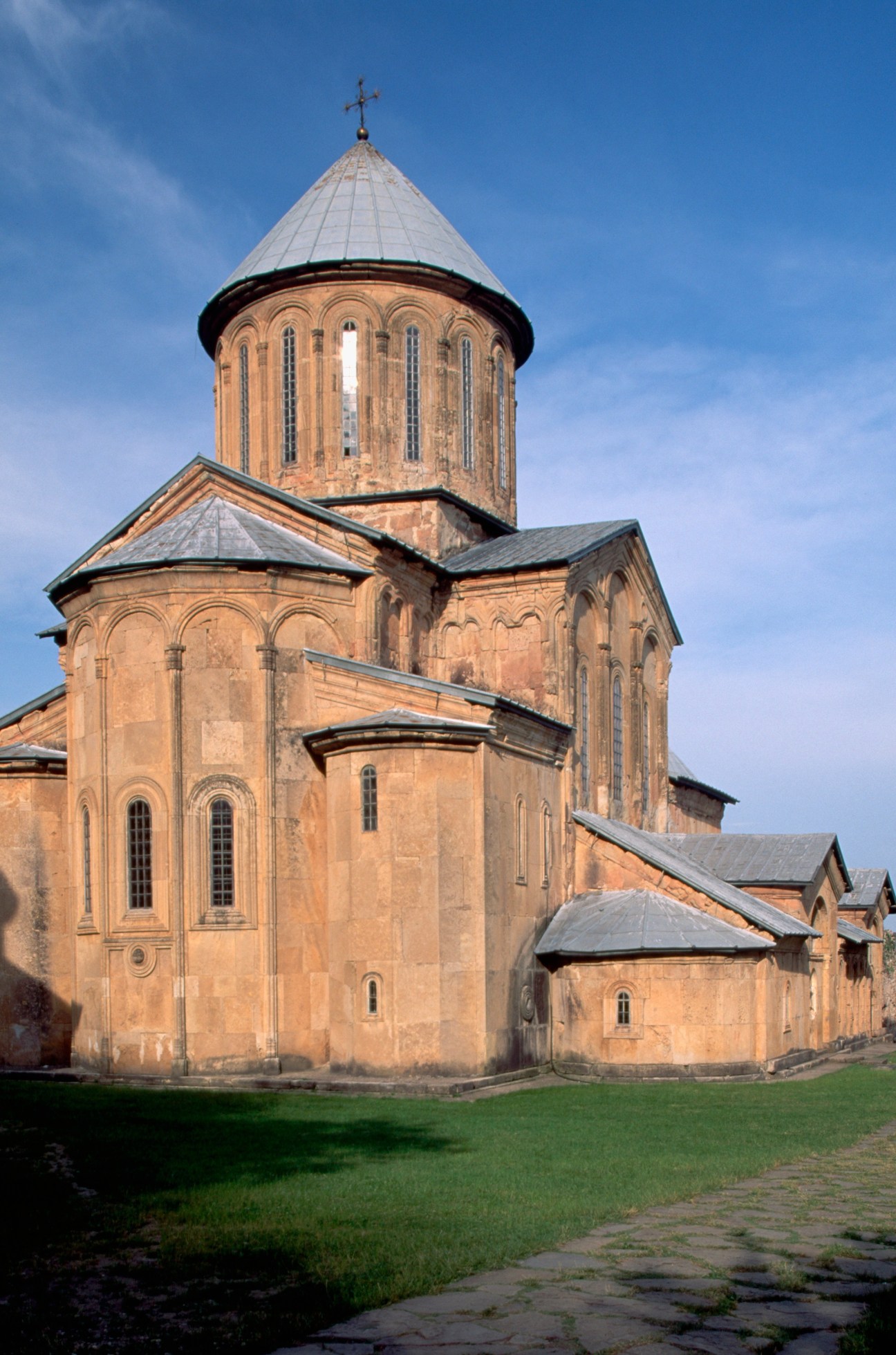 Georgian Orthodox monastery with conical tower and cross against blue sky.