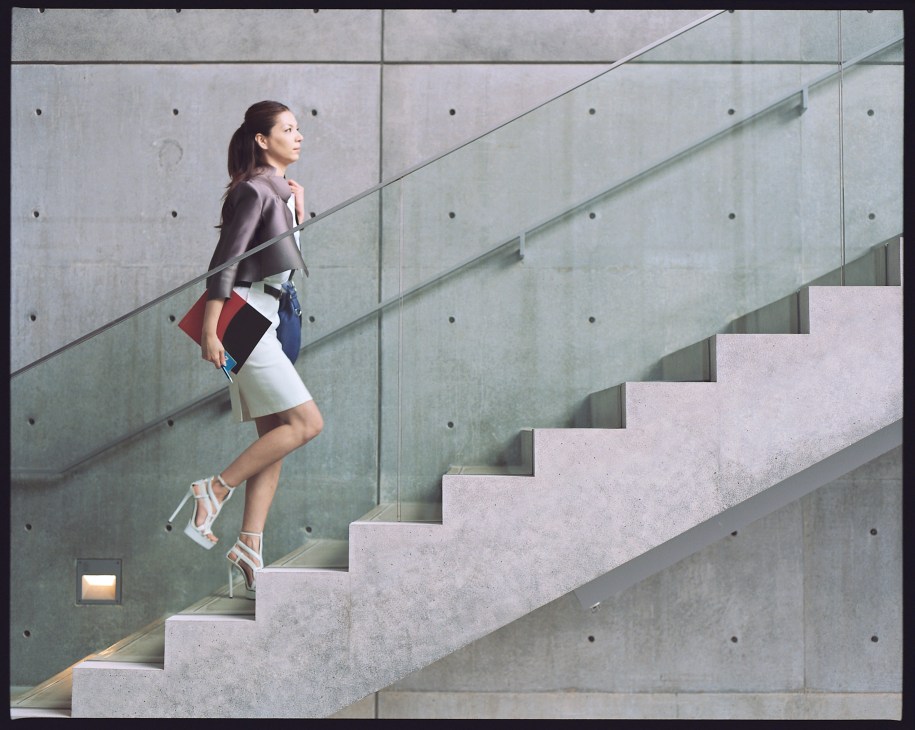 Model ascending concrete stairs wearing a Prada jacket and Ralph Lauren skirt at 21_21 Design Sight museum.
