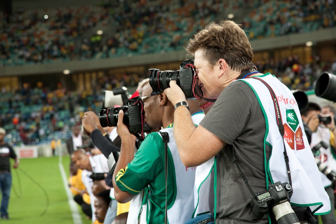 Photographers with cameras positioned along the pitch at a World Cup stadium match.