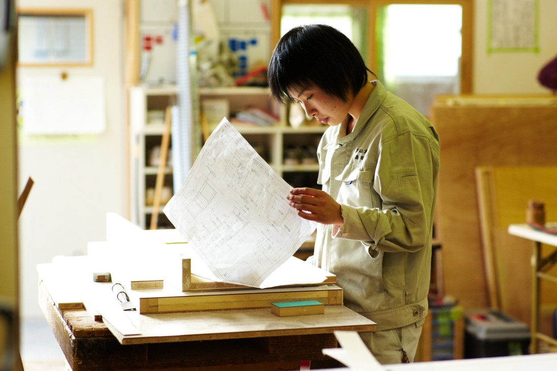 Apprentice viewing a furniture blueprint at Akiyama Mokko workshop in Yokohama.