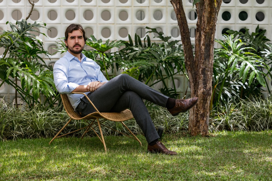 Felipe Hess sits in a wicker chair in a tropical garden setting with perforated white wall behind