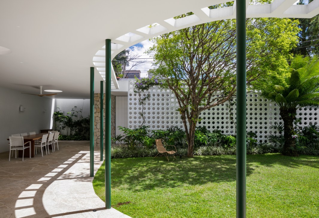 Modern veranda with white pergola, green columns, perforated wall screening garage, and outdoor dining area