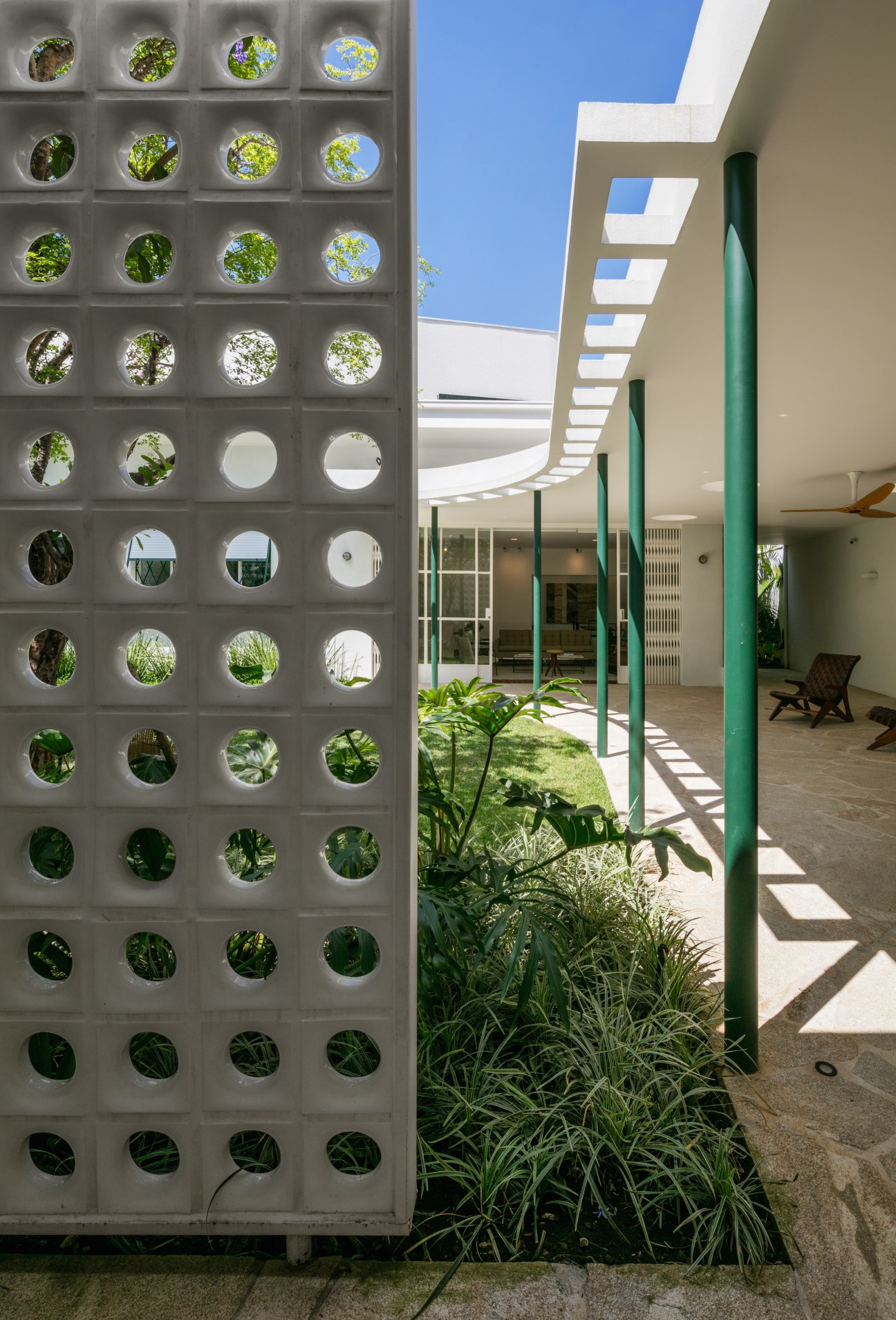 Modern home entrance featuring white perforated ceramic wall with circular holes and tropical plants beneath